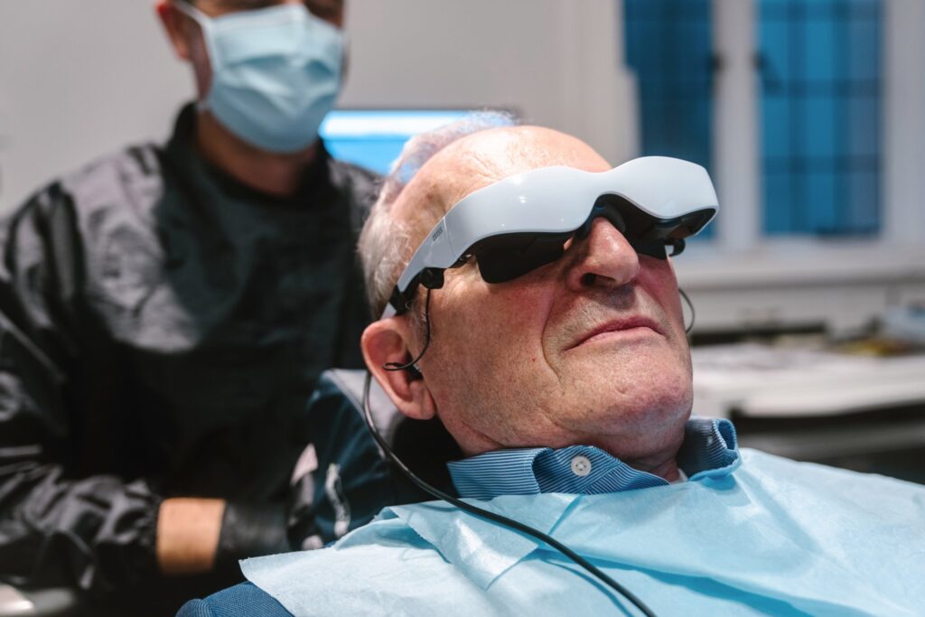 Male patient with special dental glasses on lying in the dental chair. Male endodontist in the background