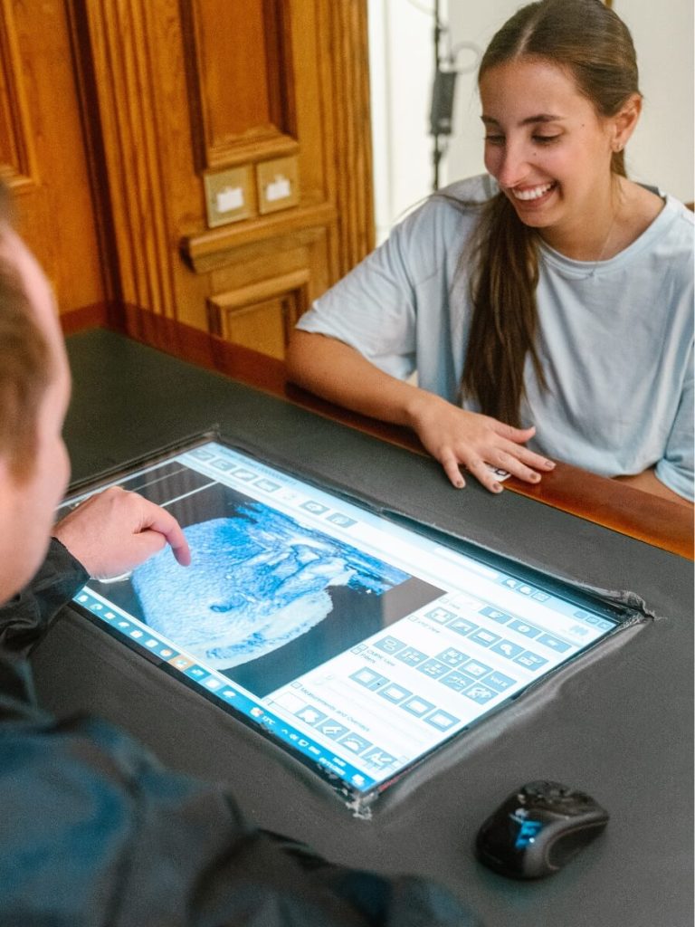 Male endodontist speaking to female patient at aa table showing her images on a computer screen. Female patient is smiling and looks happy