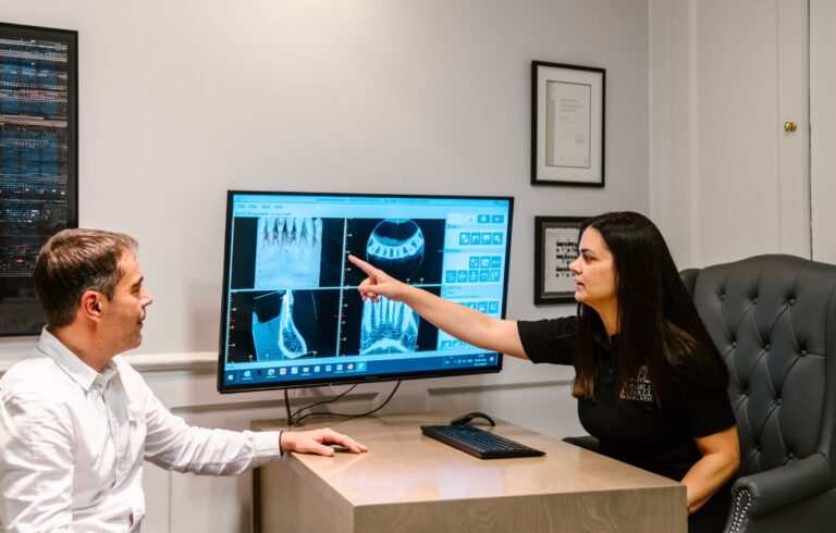 Female endodontist discussing a treatment plan with male patient and looking at tooth x-rays on a computer screen